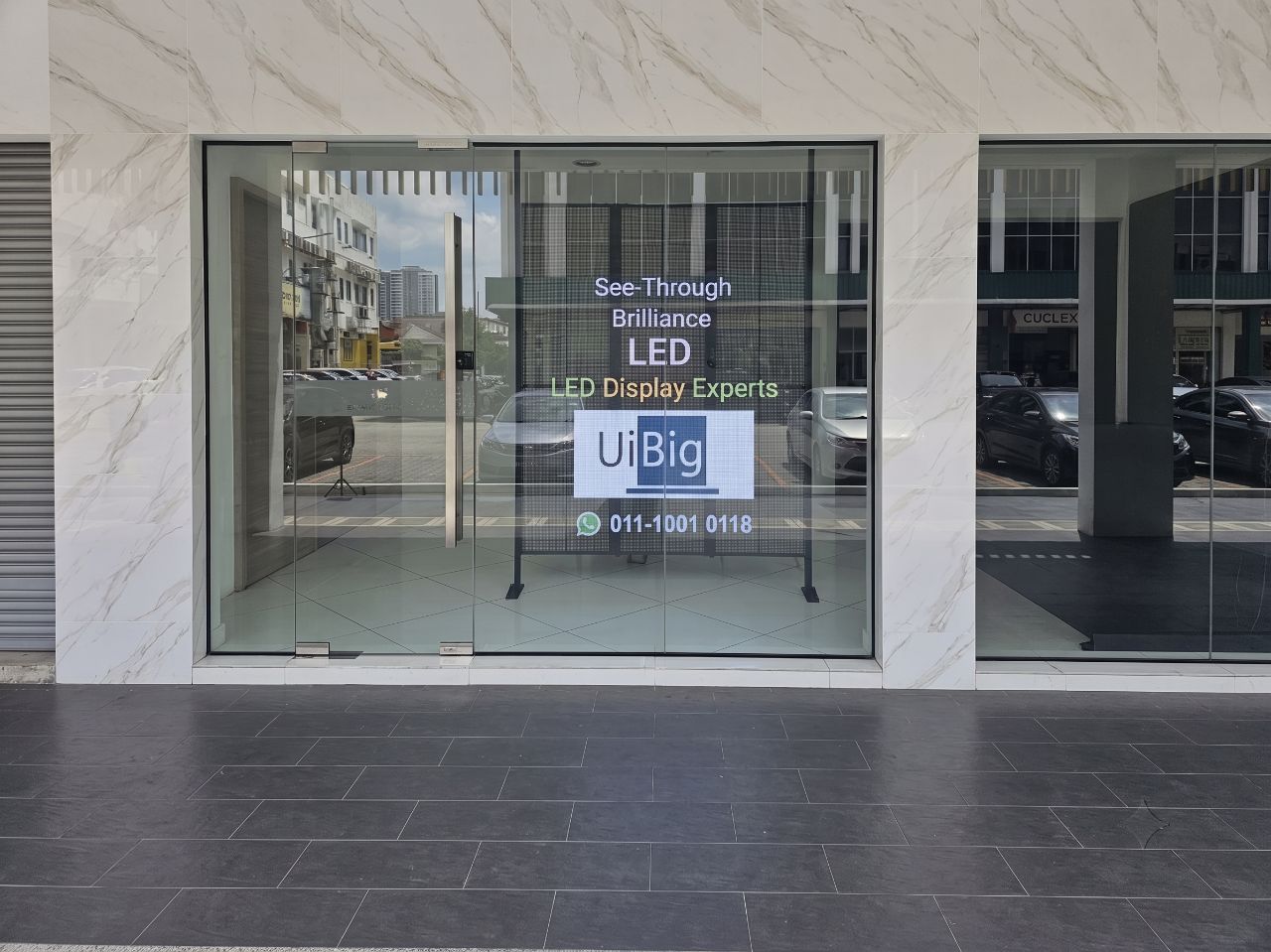 UiBig's transparent LED display on a live glass shopfront reading 'See-Through Brilliance, LED Display Experts', clear from the street in daylight